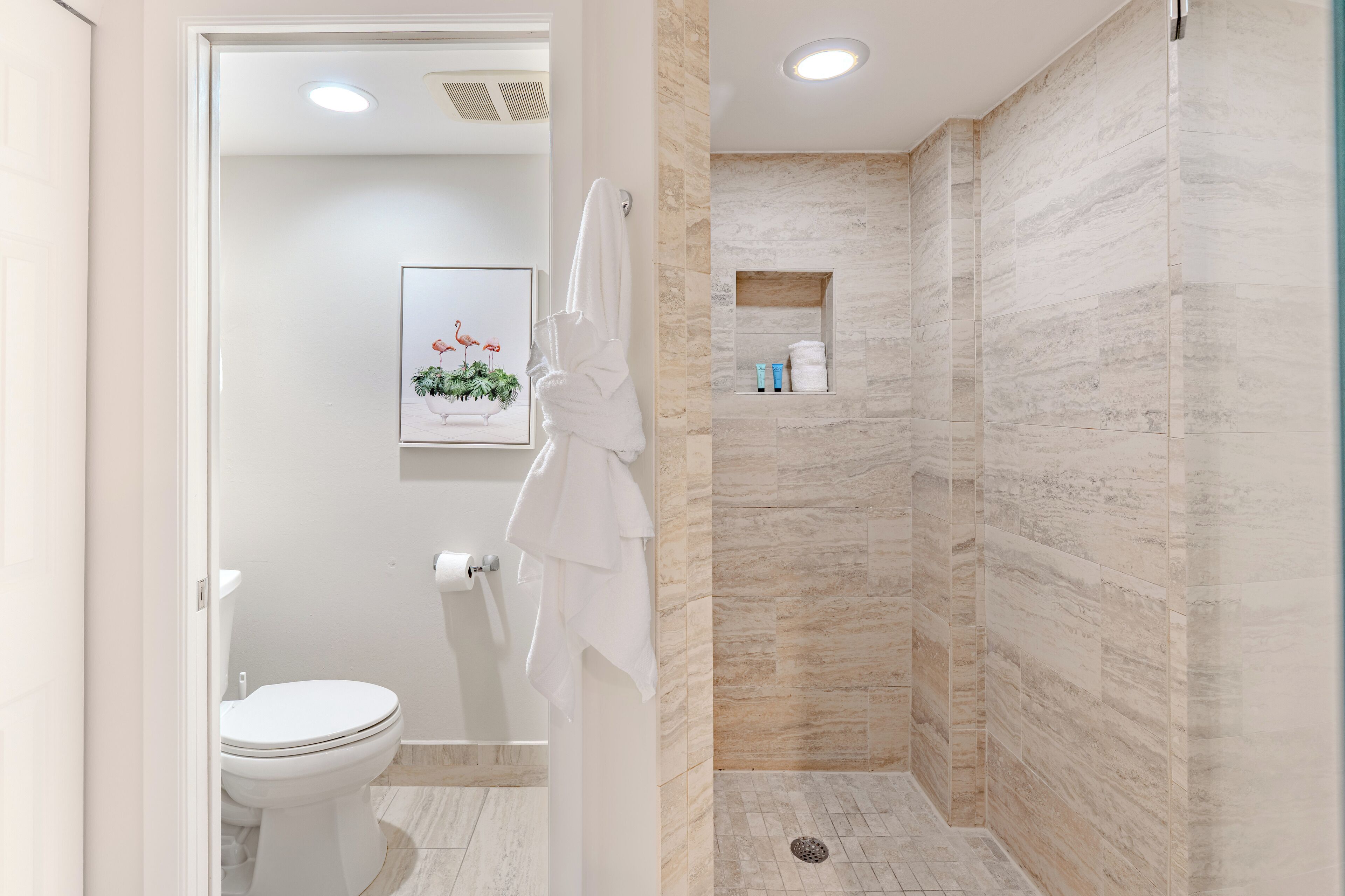 A modern bathroom with a toilet, a shower area with a glass door, and a framed picture on the wall.