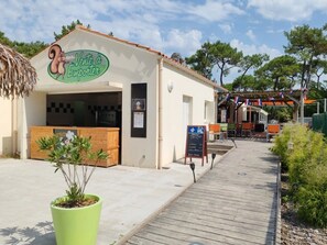 Un restaurant avec une enseigne indiquant « plats à emporter », des tables en plein air et une terrasse en bois.