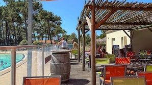 Un'area esterna con tavoli e sedie, una piscina e una struttura in legno a pergola.