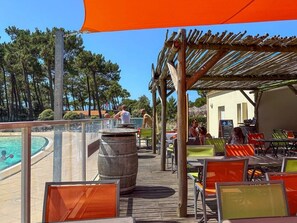 Un espace extérieur aménagé avec des tables et des chaises, une piscine et une structure en bois formant une pergola.