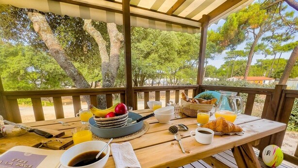 Eine Holzterrasse mit Frühstücksangebot, darunter Früchte, Croissants und Kaffee.