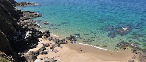 A beach with clear water, rocky shoreline, and people sunbathing.