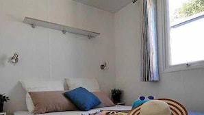Un dormitorio con cama, almohadas, un sombrero y una ventana con cortinas.