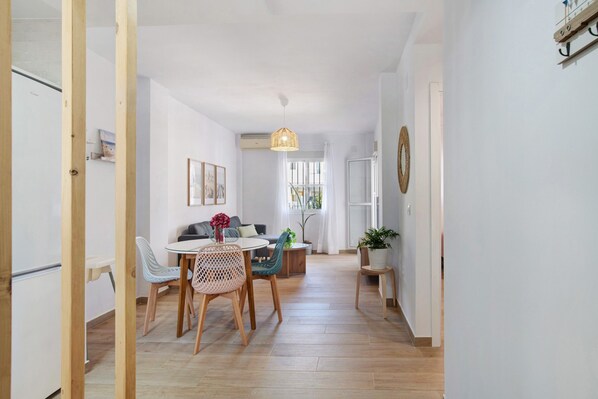 A modern interior with a dining area, a sofa, a hanging light fixture, and a potted plant.