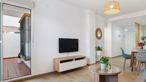 Una sala de estar moderna con televisor, mueble de madera, mesa de centro de vidrio y comedor con sillas.