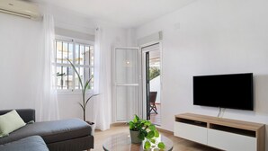 Un salón con sofá, una mesa de centro de vidrio con planta, televisor en la pared y puerta corredera que da a un espacio exterior.