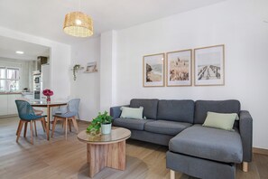A modern living room with a grey sofa, a round coffee table, and a dining area with blue chairs.