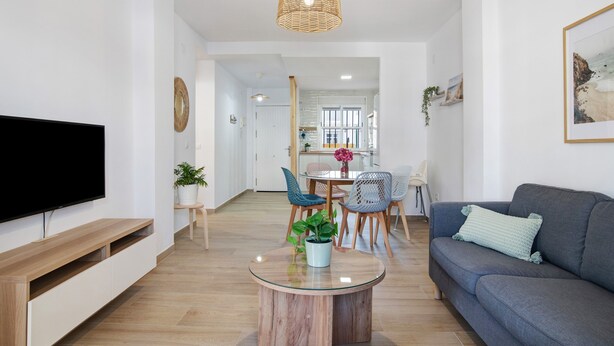 Una sala de estar moderna con un televisor de pantalla plana, un sofá, una mesa de centro y un comedor con sillas y una mesa.