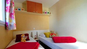 A compact room with two beds, a small desk, and a window with curtains.