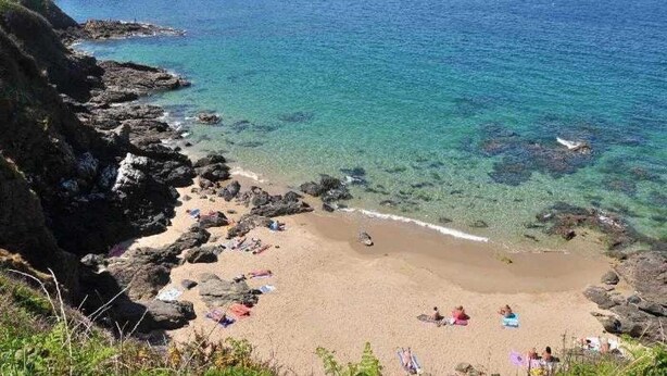 A beach with clear water, rocky shore, and people sunbathing.