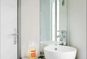 A bathroom with a white sink, a mirror, and a bottle of hand soap. - ZEcamping 4 étoiles familial parc aquatique locatif TV BBQ 29m2 (Saint-Lunaire)
