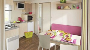 Eine kleine Küche mit Mikrowelle, Herd und Spüle. Es gibt einen Essbereich mit einem für zwei gedecktem Tisch und ein rosafarbenes Sofa.
