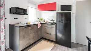 Eine kleine Küche mit Mikrowelle, Herd und Kühlschrank, mit einem roten Oberschrank und einem kleinen Fenster.