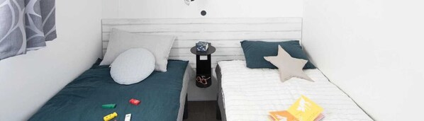 Una habitación pequeña con cama individual, cabecero blanco, mesita de noche con lámpara y una almohada con forma de estrella.