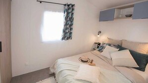 Ein Schlafzimmer mit einem Bett, einem Fenster mit Vorhängen, einem Nachttisch und einem Regal über dem Bett.