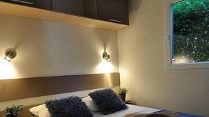 Ein Schlafzimmer mit Bett, Nachttischen, an der Wand befestigten Schränken und einem Fenster mit Blick auf Grünflächen.