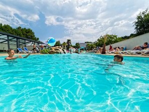 Una piscina con agua azul cristalina, sillas de descanso y un tobogán.