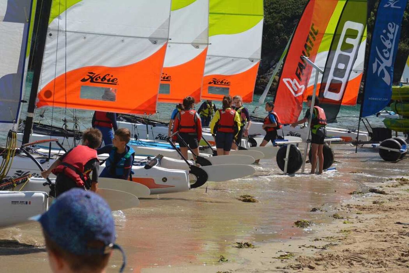 Un groupe de personnes prépare des voiliers sur une plage de sable.