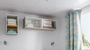 En snyggt bäddad säng med ett brickbord med två muggar, ett litet bord bredvid och ett fönster med mönstrade gardiner.