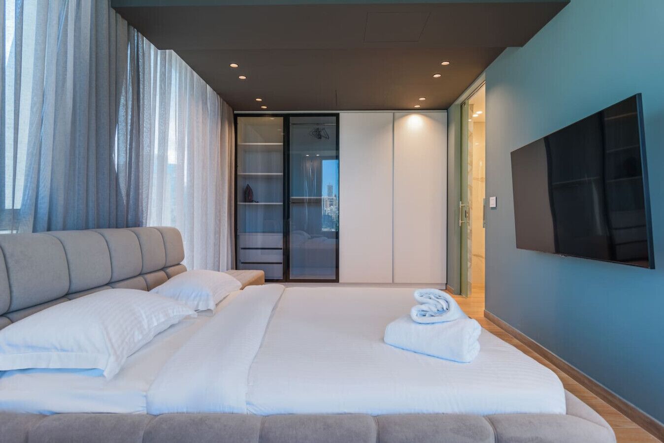 Une chambre moderne avec un grand lit, un canapé, une porte-fenêtre coulissante et un téléviseur à écran plat fixé au mur.
