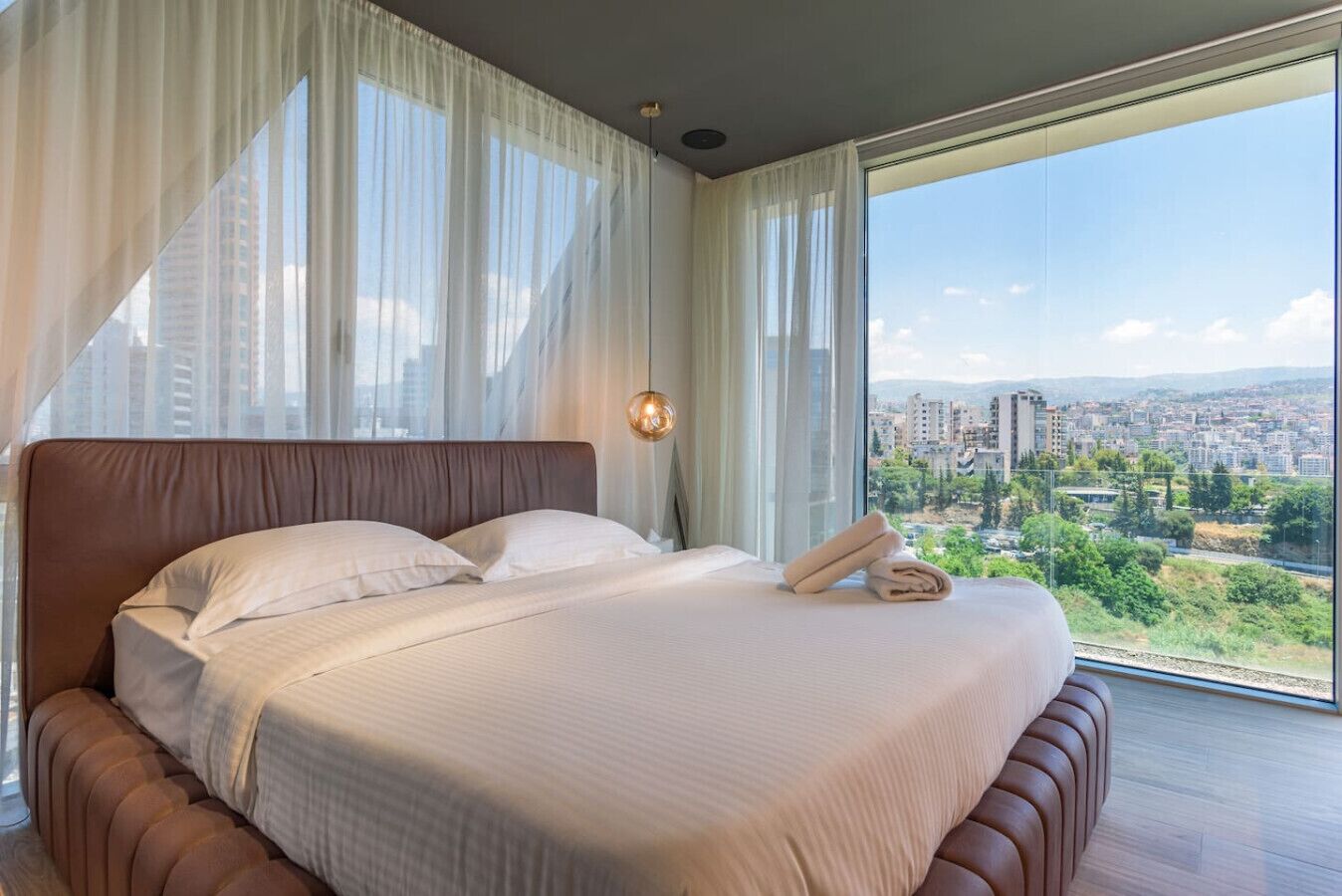 Un dormitorio moderno con una cama grande, cortinas translúcidas y vistas a la ciudad.