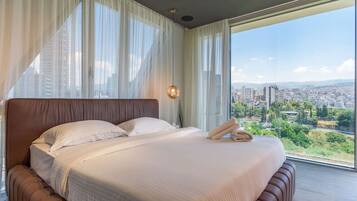 Un dormitorio moderno con una cama grande, cortinas translúcidas y vistas a la ciudad.