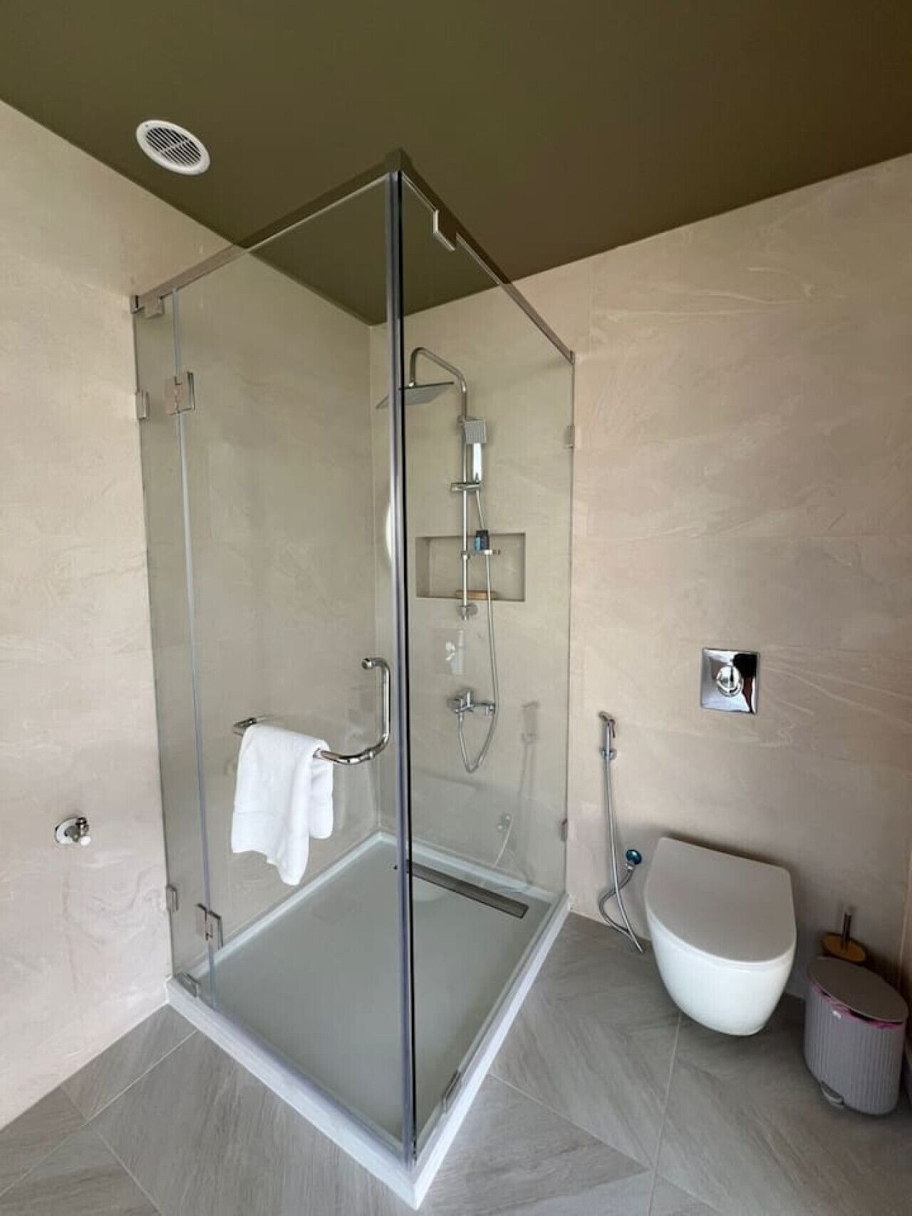 Un bagno moderno con cabina doccia in vetro, un water bianco e un piccolo cestino.