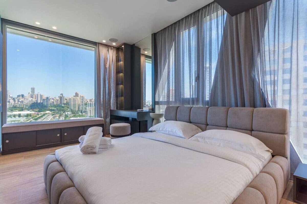 A modern hotel room with a large bed, a seating area, and a city view.