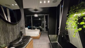 Une salle de bain moderne avec un grand miroir, un lavabo noir, un meuble-lavabo en bois et une baignoire noire.