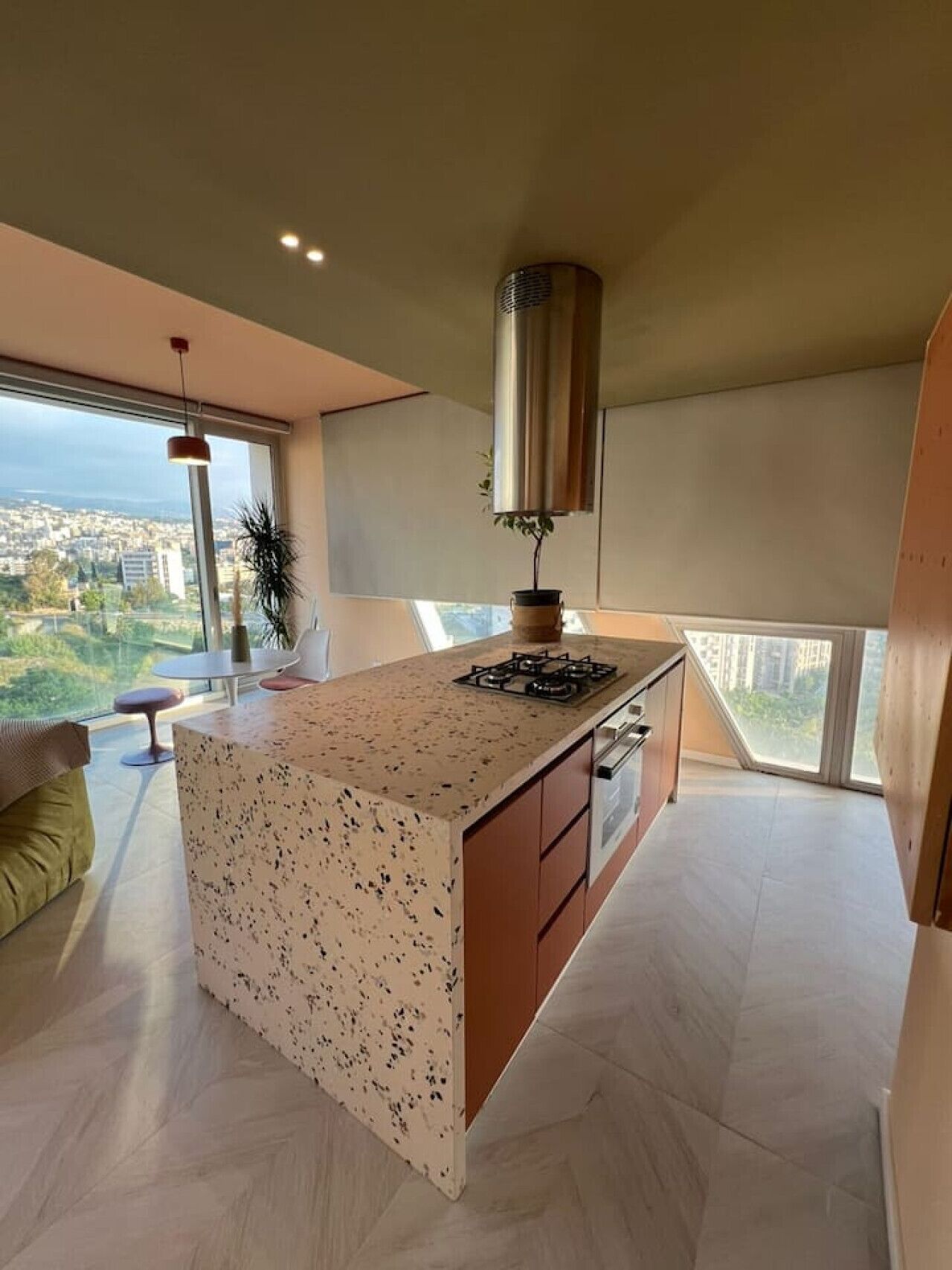 A modern kitchen with a central island, a gas stove, and a view of the city through large windows.