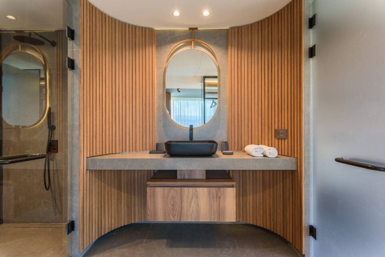 A modern bathroom with a curved vanity, a round mirror, and wooden paneling.