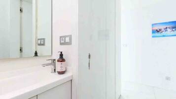 Un bany amb un lavabo blanc, un mirall, una ampolla de sabó i una porta.