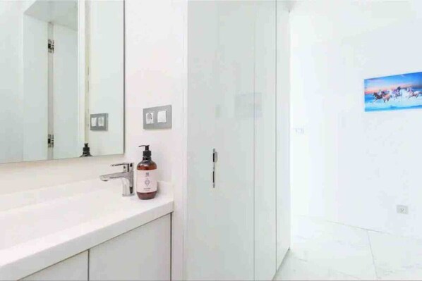 Un bagno con un lavandino bianco, uno specchio, una boccetta di sapone e una porta.