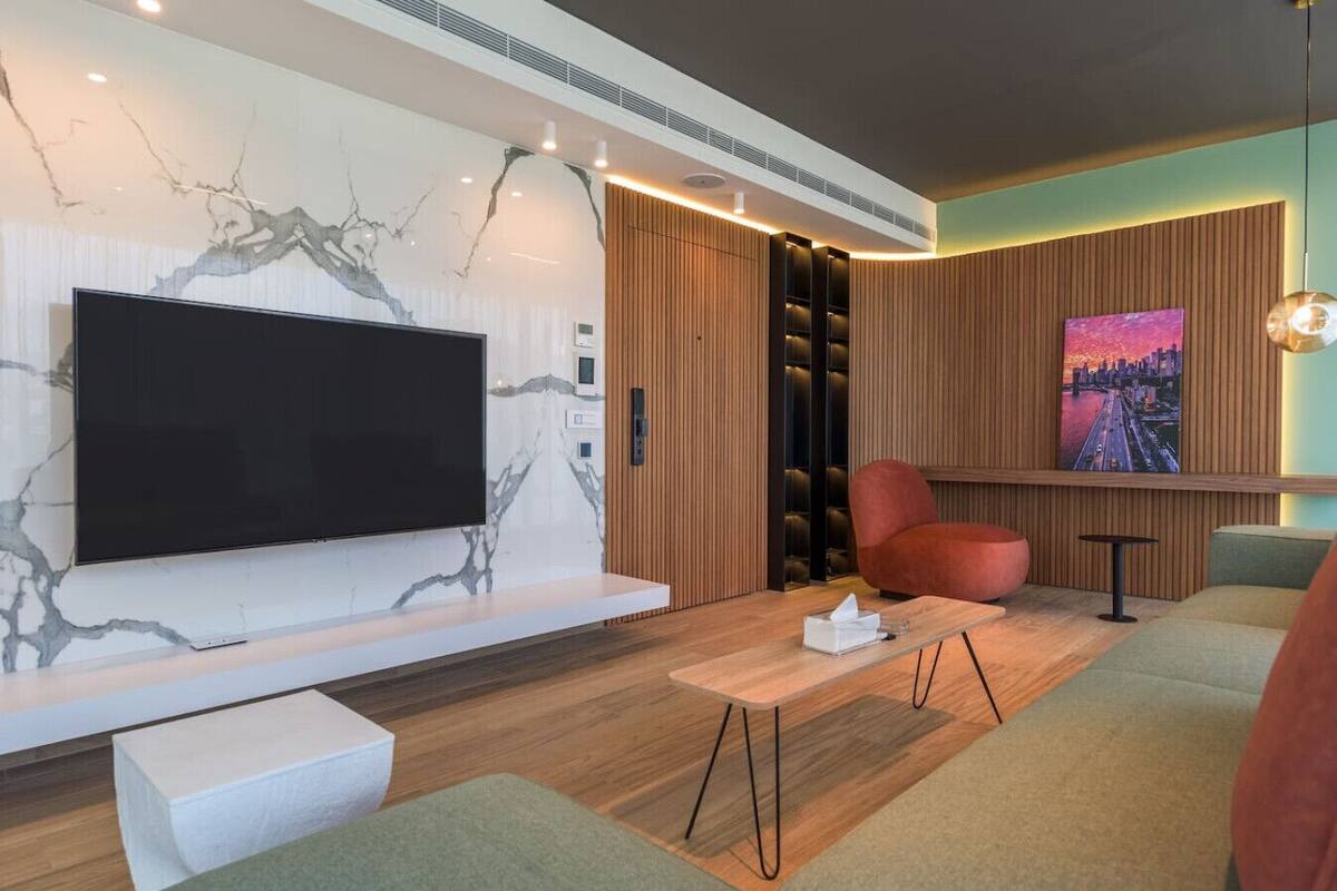 A modern living room with a large flat-screen TV, wooden paneling, a red armchair, and a cityscape painting.