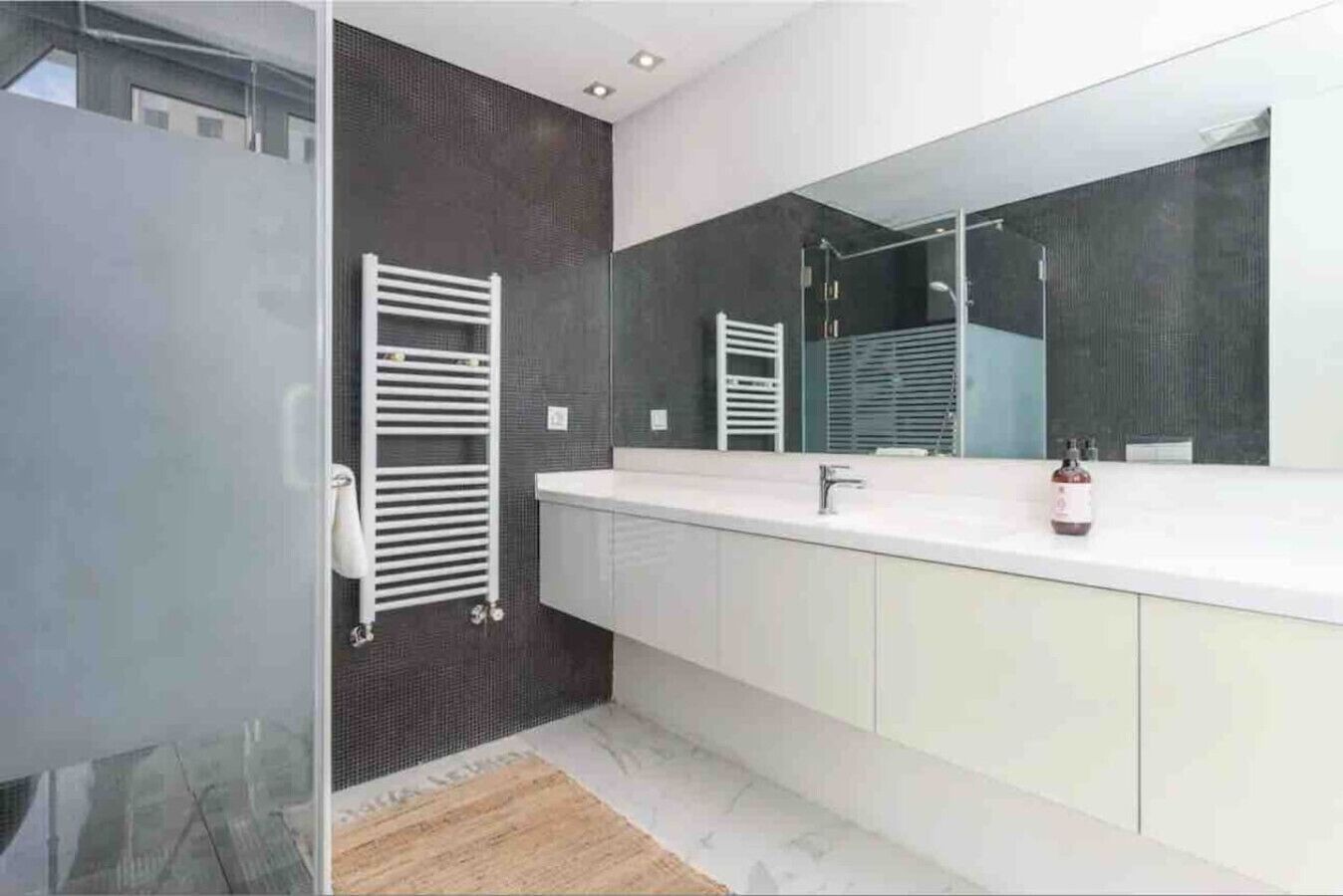 Un baño moderno con un espejo grande, tocador blanco y un perchero para toallas.