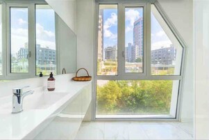 Un baño moderno con un ventanal grande, un lavabo blanco y un espejo.