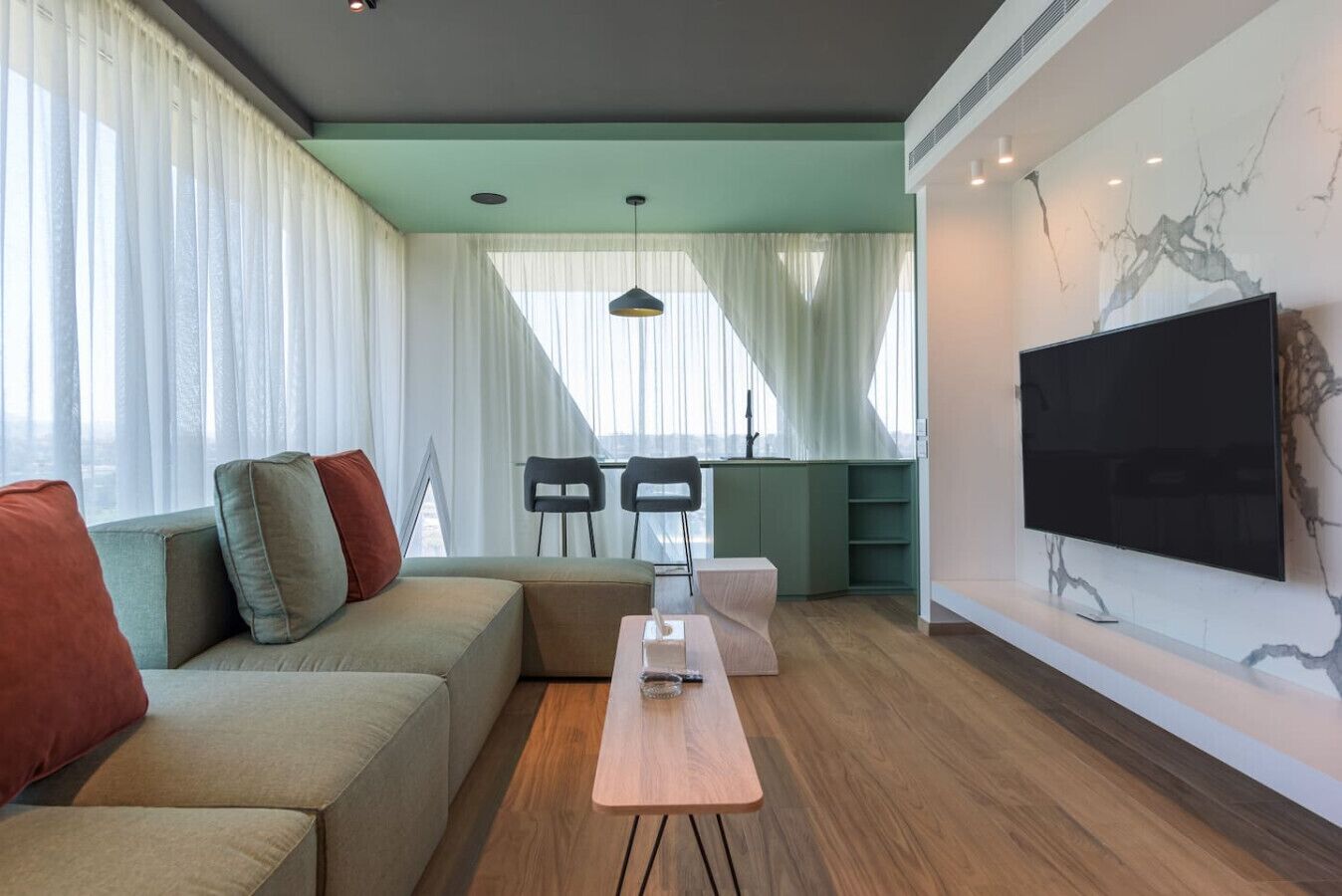 A modern living room with a sectional sofa, a coffee table, and a flat-screen TV mounted on the wall.