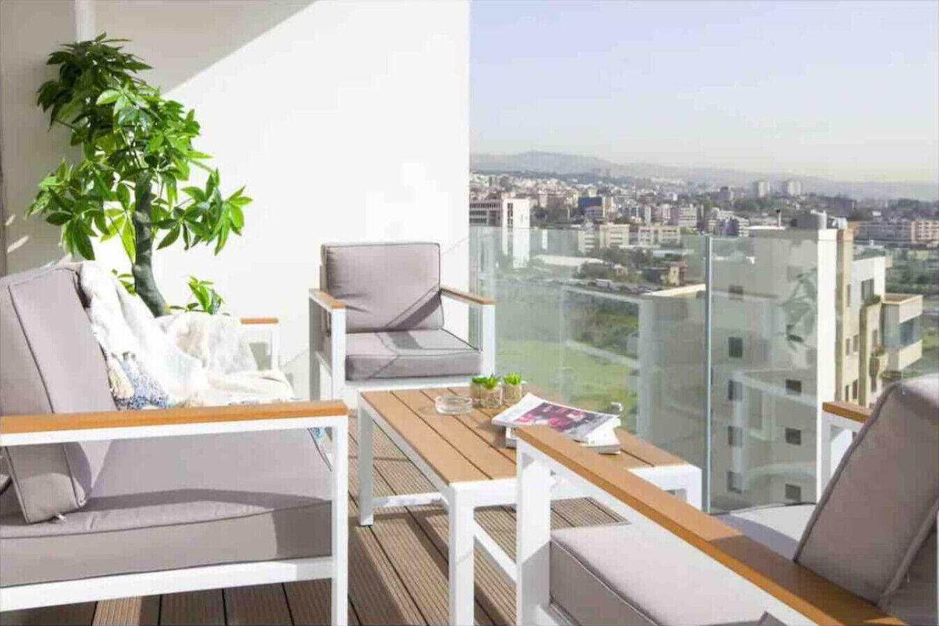 A balcony with a view of a cityscape, a potted plant, and a table with a magazine.