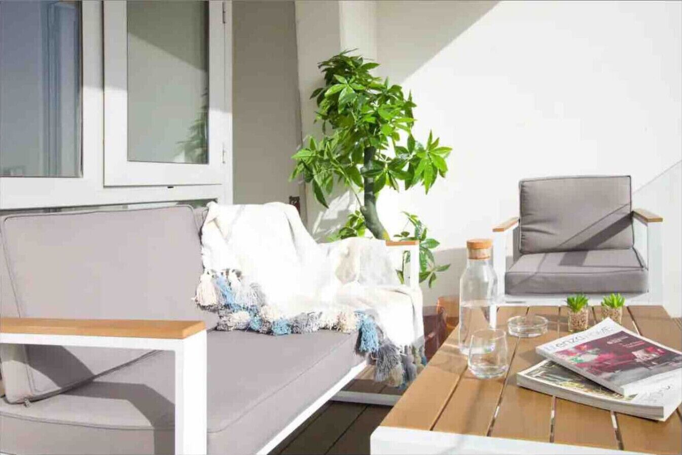 A modern outdoor seating area with a sofa and chairs, a table with a magazine and a water bottle, and a potted plant.