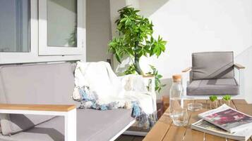 A modern outdoor seating area with a sofa and chairs, a table with a magazine and a water bottle, and a potted plant.