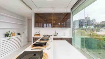 A modern kitchen with a long countertop, wooden cabinets, and a view of the city through large windows.