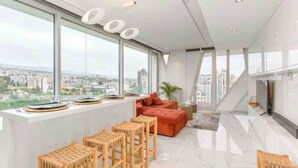 Un salon moderne avec vue sur la ville, un canapé, des tabourets en bois et une grande fenêtre.