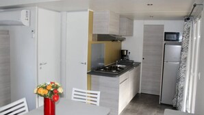 A compact kitchen with a gas stove, microwave, and refrigerator. There is a dining table with a vase of flowers.