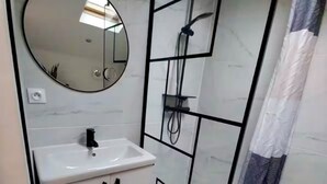 A modern bathroom with a round mirror, a sink, a shower enclosure, and a toilet.