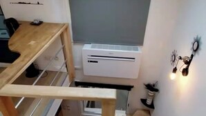 A compact room with a skylight, built-in air conditioning unit, and a wooden desk with shelves.