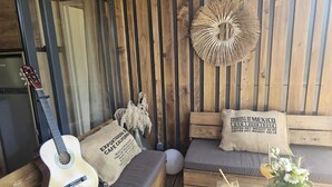 Un espacio al aire libre acogedor con una guitarra, un adorno de pared tejido y una mesa con bebidas y flores.