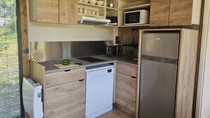 Cocina compacta con armarios de madera, microondas, refrigerador, lavavajillas y ventana con persianas.