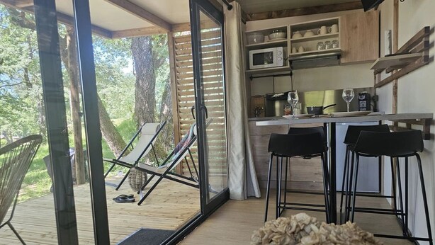 Una cocina moderna con una isla grande, un comedor con taburetes de bar y un puerta corrediza de vidrio que da a una terraza exterior con una silla y un columpio.