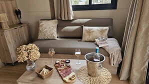 Una sala de estar acogedora con un sofá, cojines, una mesita de centro con aperitivos y bebidas, y una ventana con cortinas.