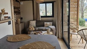 Una habitación acogedora con cama, un banco de madera, una mesa de comedor con sillas y un amplio ventanal con vistas al exterior.